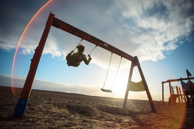 Low angle view of woman swinging at playground against sky during sunset