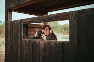 Young woman taking photos in a wooden hide with an old analog camera