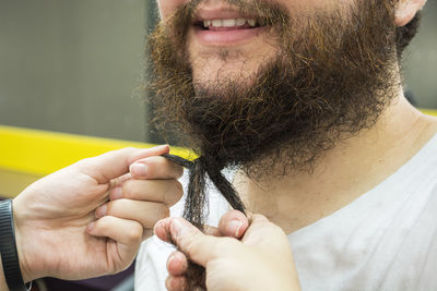 Cropped hands of person tying beard of man