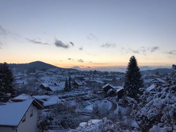 Snow covered houses and trees against sky during sunset