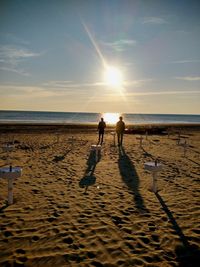 Silhouette people walking on beach against sky during sunset