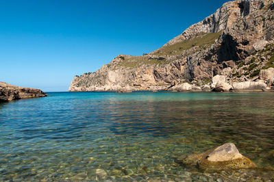 Rock formations in sea against clear blue sky