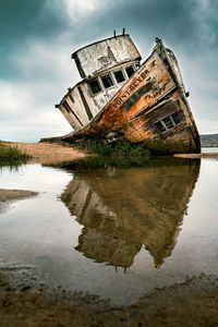 Abandoned building by lake against sky
