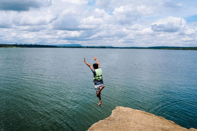 Rear view of man jumping in sea against sky