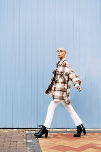 Young woman with shaved head walking on footpath by blue wall