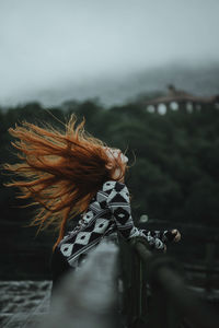 Side view of redhead woman tossing hair while leaning on railing