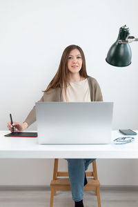 Pretty graphic designer or retoucher sitting at the table with laptop and looking into camera. 