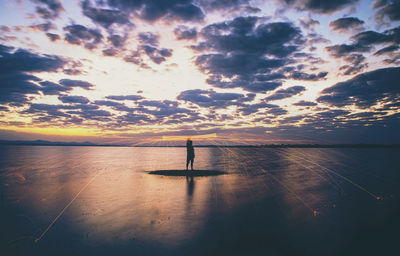 Silhouette person standing in sea against sky during sunset