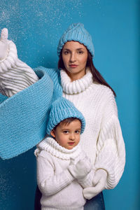 Mother and son in white sweaters and blue hats stand on a blue background in the studio