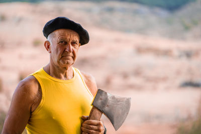 Portrait of senior man with axe standing in forest