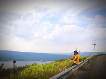 Portrait of smiling woman sitting on railing against cloudy sky