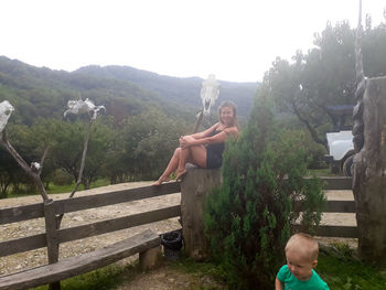 Rear view of shirtless boy sitting on plants against sky