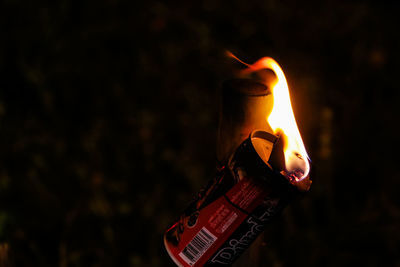 Close-up of hand holding lit candle against black background