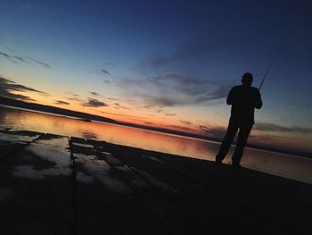 Silhouette man standing by sea against sky during sunset