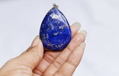 Close-up of woman hand holding gemstone against white background