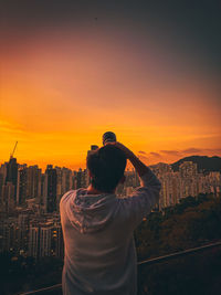 Rear view of man standing by buildings against sky during sunset