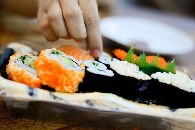 Cropped hand taking sushi served in plate