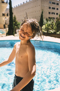 Smiling shirtless boy enjoying by swimming pool in resort