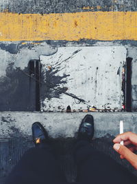 Low section of man holding cigarette while standing on sidewalk