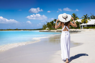 Rear view of woman standing at beach against sky