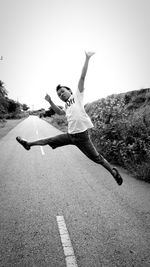 Full length of man jumping on road against clear sky