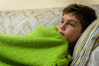 Boy looking away while relaxing on sofa at home