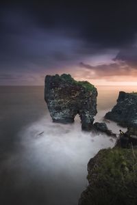 Rock formation in sea against sky during sunset