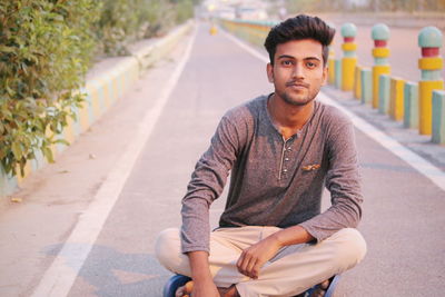 Portrait of smiling young man sitting on road