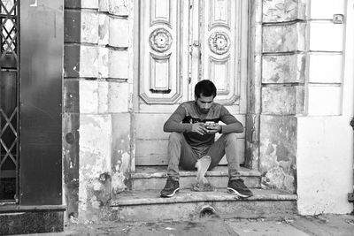 Full length of young man sitting at entrance of building