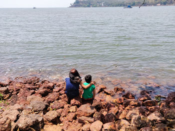 Rear view of family sitting on rock by sea