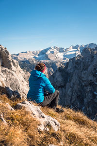 Rear view of person on rock in mountains against blue sky