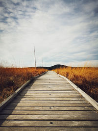 Surface level of dirt road on field against sky