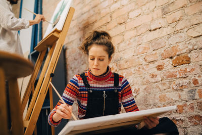 Low angle view of female and male artists painting on canvas at art studio