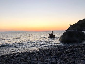 Silhouette rocks on sea against sky during sunset