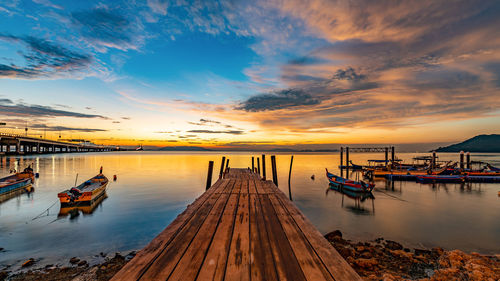 Fishing boats moored in sea against sky during sunset