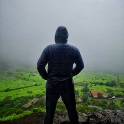 Rear view of man standing on cliff against sky