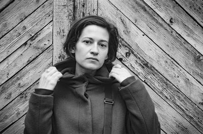 Portrait of young woman standing against wooden wall