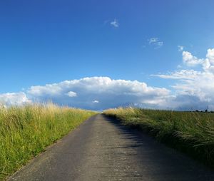 Road amidst field against blue sky