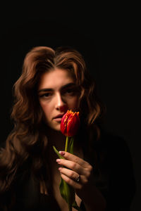 Close-up of woman holding red rose against black background