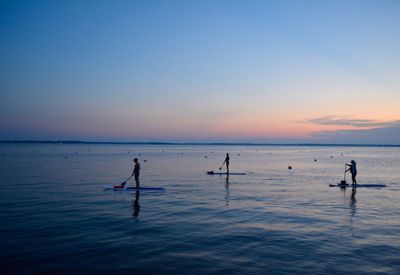 People in sea against sky during sunset