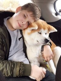 Boy sitting with arm around akita in car