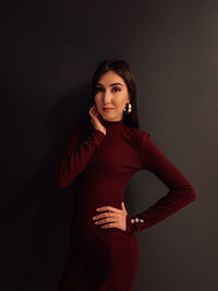 Portrait of young woman standing against black background