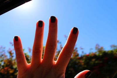 Cropped hand of woman with black nail polish against clear sky