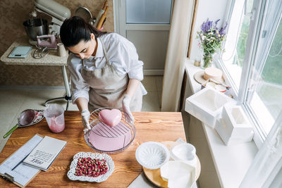 Female baker make perfect custom pink heart shape cake in kitchen bakery. online cake store. custom