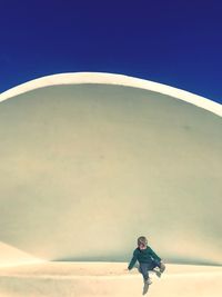 Boy sitting in built structure against sky