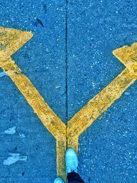 Low section of person standing on arrow sign on road