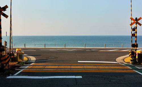 Road and railroad crossing by sea against clear sky