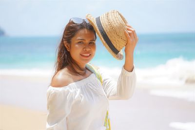 Portrait of beautiful young woman standing at beach against sky