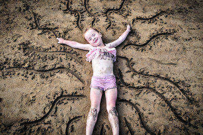 High angle portrait of happy girl lying on sand at beach