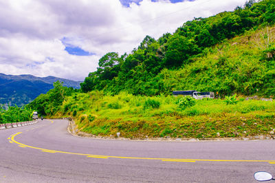 Road amidst trees and mountains against sky